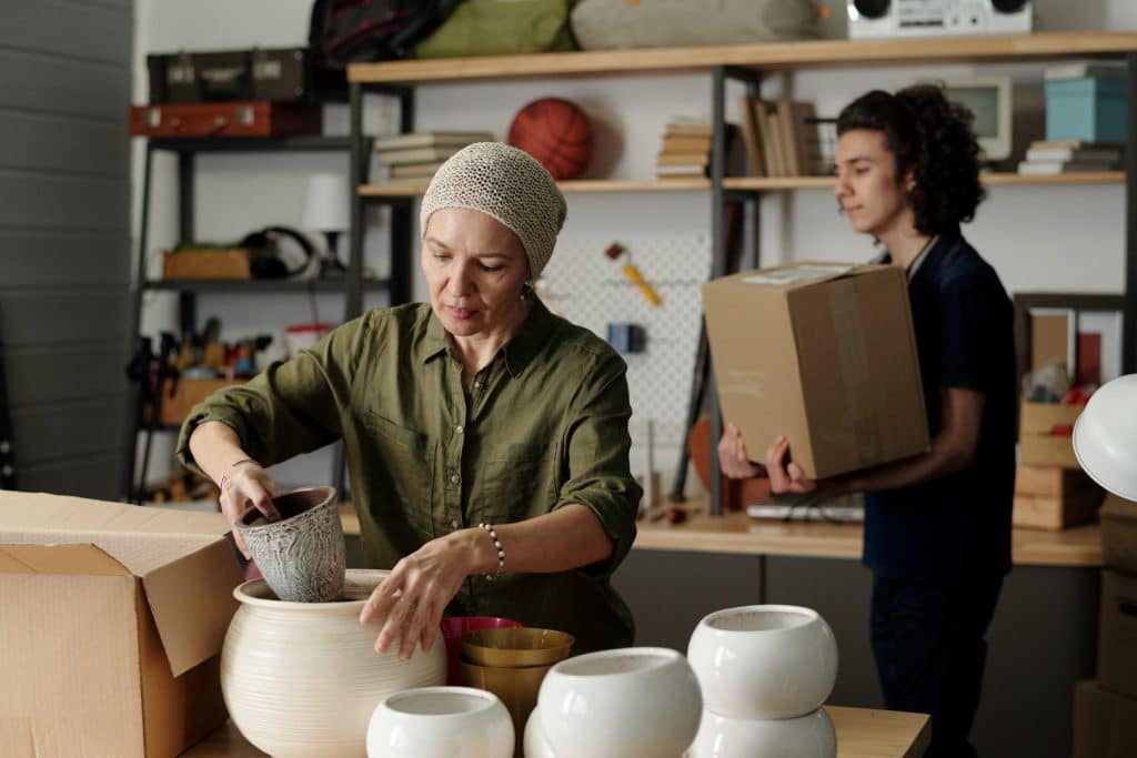 Woman packing flowerpots in the garage while young man carries cardboard box
