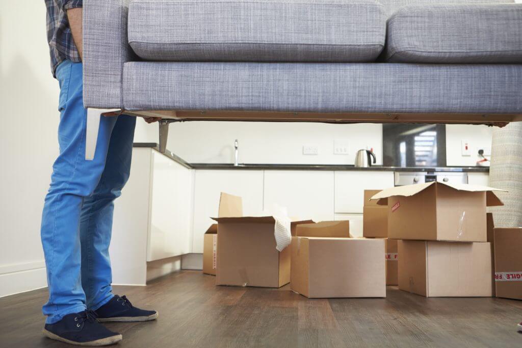 Close Up Of Man Carrying Sofa As He Moves Into New Home