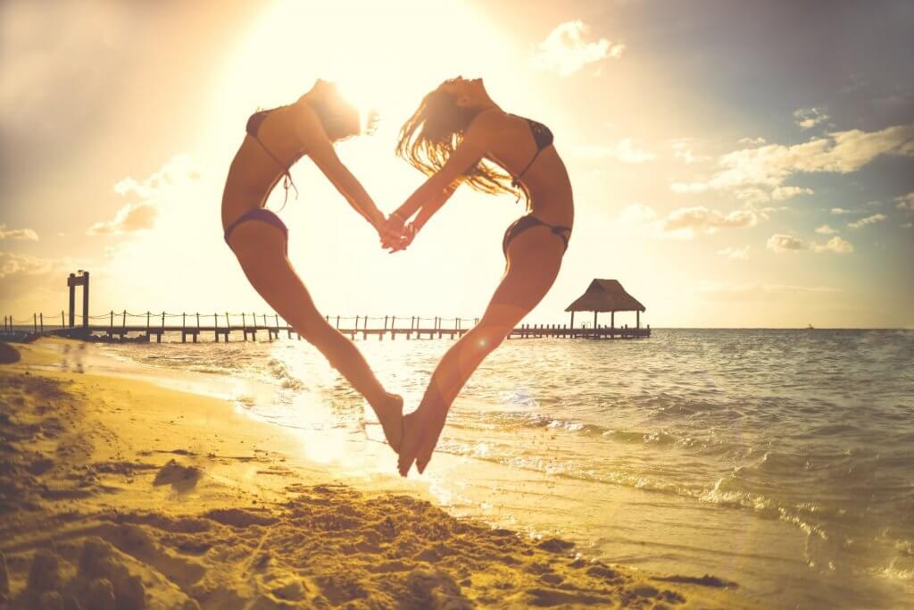 Two women jumping making a heart shape at the beach.