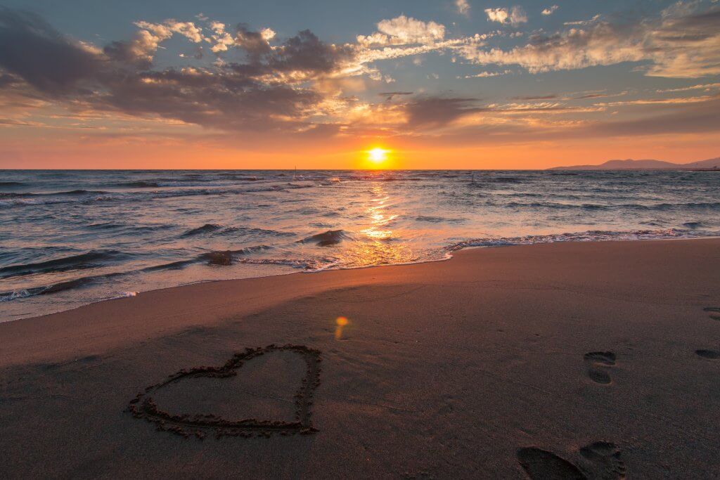 Hearts drawn in the sand by a beach at sunset.