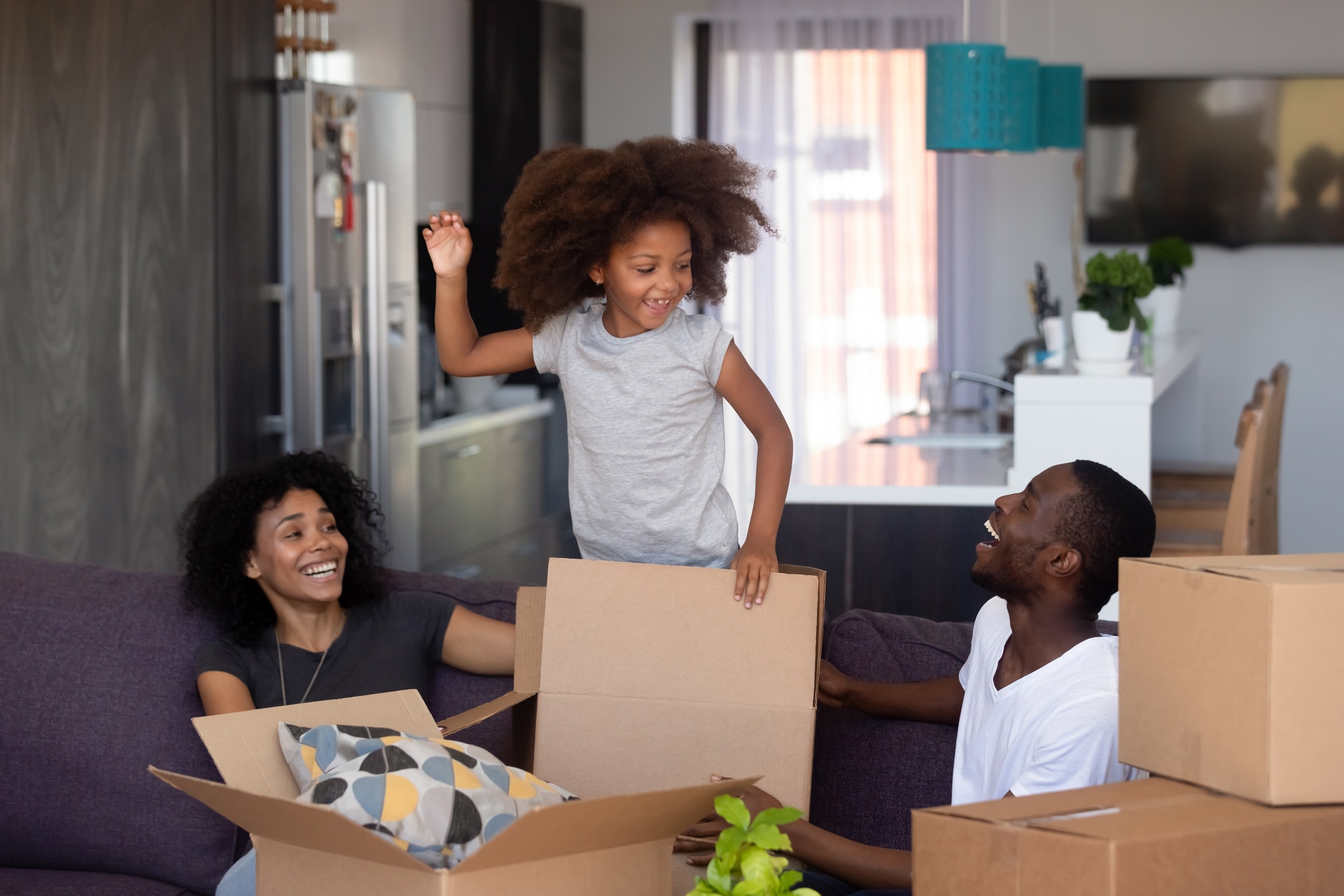 Family packing boxes. A little girl is standing in a box and her parents are smiling