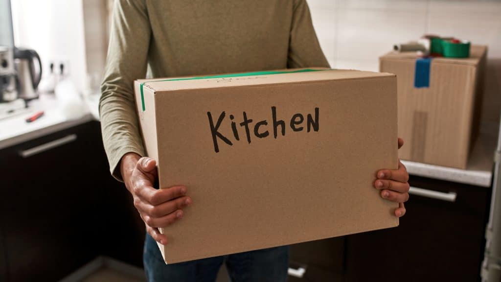 Man carrying a box labeled 'kitchen' during his small move